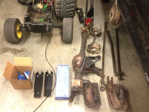 1979 Ford Bronco - Various vehicle components and a lawnmower chassis are spread across the floor, suggesting a repair or parts project.