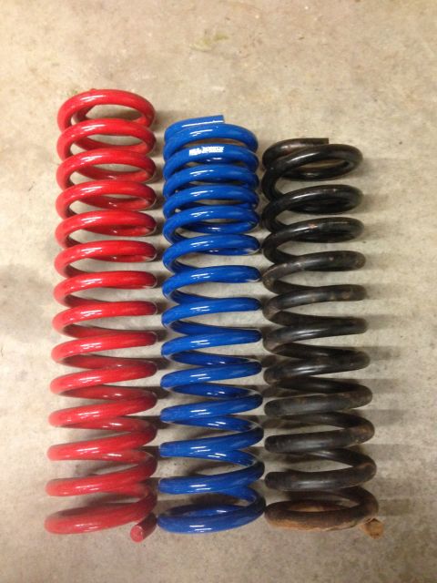 1979 Ford Bronco - Three sets of suspension springs, red, blue, and black, are displayed on a concrete floor.