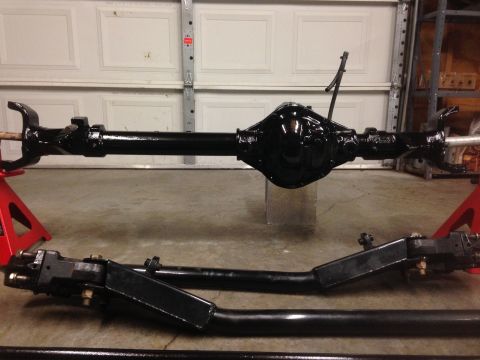 1979 Ford Bronco - A black painted front axle assembly with its differential housing is shown, supported by red jack stands in a garage.