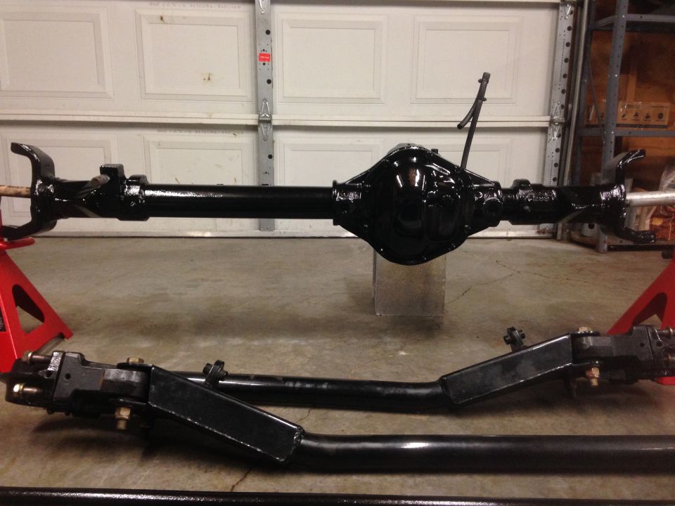 Black painted front axle assembly with differential housing and steering components, resting on red jack stands