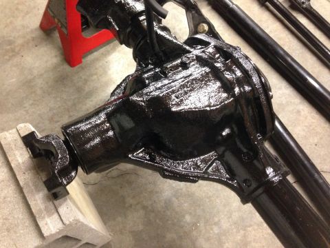 1979 Ford Bronco - A black differential housing is shown, resting on a concrete floor with a red jack stand and blocks for support.