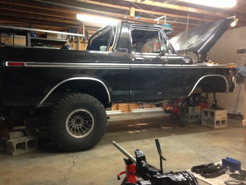1979 Ford Bronco - This black Ford Bronco is raised on jack stands inside a garage, with its hood open for maintenance.