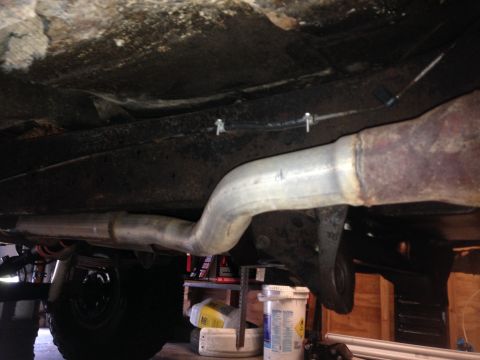 1979 Ford Bronco - Close-up view of the exhaust system and undercarriage, showing suspension parts and some stored items in the background.