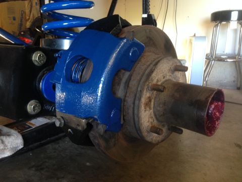 1979 Ford Bronco - Close-up of a vehicle's suspension components, including a freshly painted brake caliper and a new coil spring.