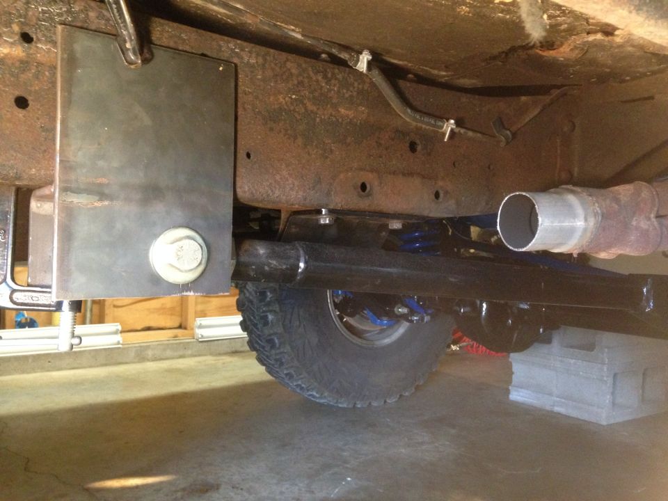 Undercarriage view showing suspension components, exhaust pipe, and a tire. A metal plate is clamped to the frame