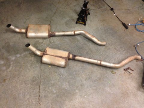 1979 Ford Bronco - Two exhaust system components are laid out on a concrete floor, with a jack stand in the background.