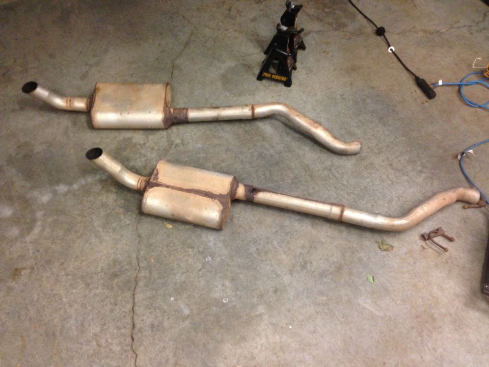 two rusty exhaust pipes and mufflers on a concrete floor