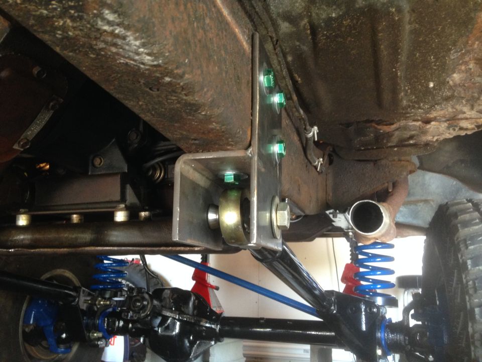Close-up of custom suspension bracket bolted to vehicle frame, showing new springs and axle components