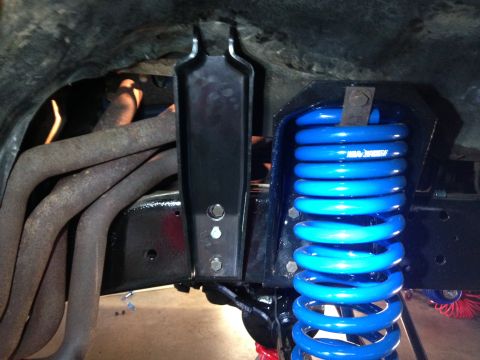 1979 Ford Bronco - Close-up view of vehicle suspension parts, including a bright blue coil spring and exhaust manifold.