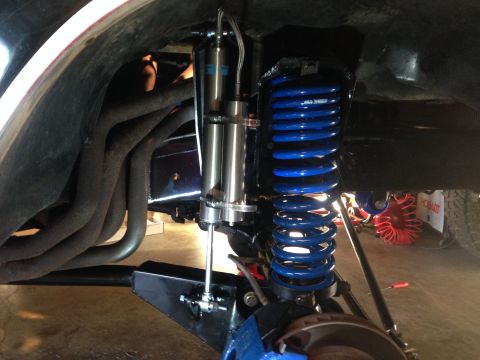 1979 Ford Bronco - Vehicle suspension upgrade blue coil springs and a shock absorber, with exhaust headers in view.