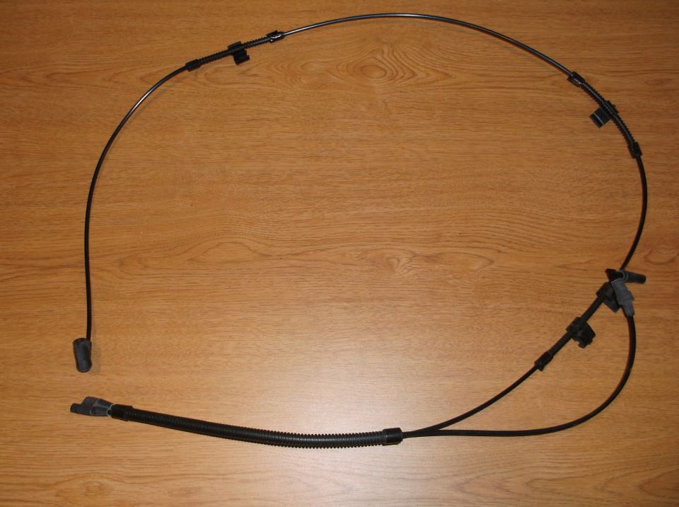 Black emergency or parking brake cable assembly laid out on a wood-grain surface