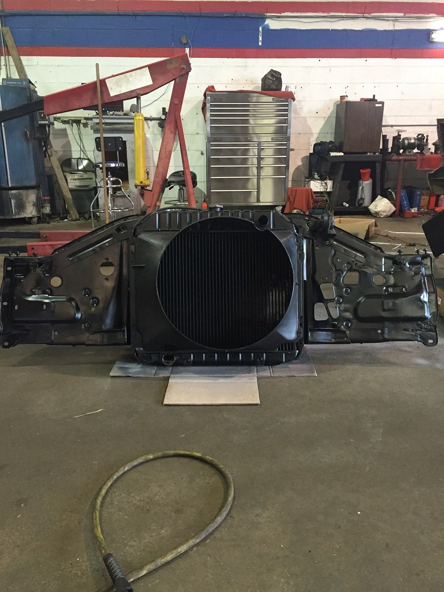 Radiator and front clip assembly removed from a vehicle, resting on the floor of a garage