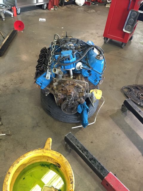 1978 Ford Bronco - V8 engine with blue valve covers and black exhaust manifolds, resting on a tire in a garage.