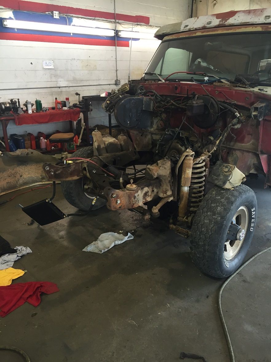 Truck front end disassembled in a garage, engine bay empty, suspension parts visible