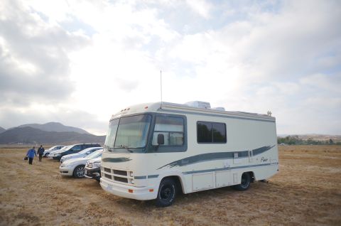 1995 Chevrolet P30 1 Ton - Step Van - This RV, with its distinctive cream and green exterior, is parked in a dry, grassy field alongside several other vehicles.