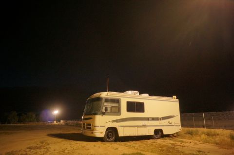 1995 Chevrolet P30 1 Ton - Step Van - A motorhome sits parked in a dirt lot under a dark night sky, illuminated by a nearby light.