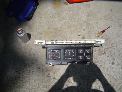 1986 Ford Bronco - A removed vehicle instrument cluster sits on a concrete surface next to a spray can and screwdriver.