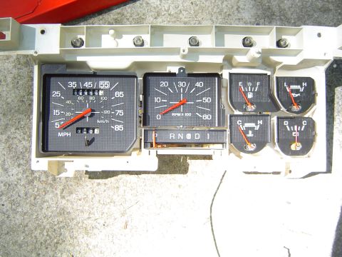 1986 Ford Bronco - A collection of automotive gauges, including a speedometer and tachometer, are laid out on a white backing.