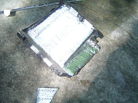 1986 Ford Bronco - An automotive part, possibly an AC component, is covered in reflective insulation and placed on a concrete surface.