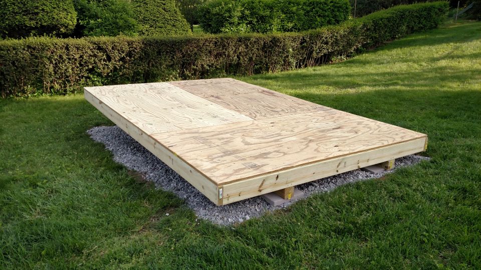 plywood platform on gravel base in grassy yard with hedges behind