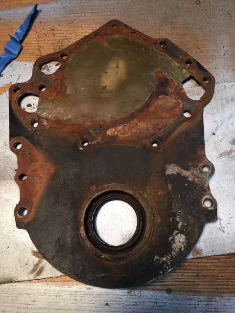1978 Ford Bronco - This heavily rusted engine timing cover is shown on a workbench, with blue tape in the upper left corner.