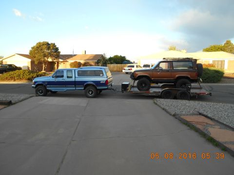 1996 Ford F-250 - A blue Ford F-250 tows a brown Ford Bronco on a trailer in a suburban driveway.