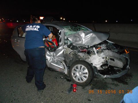 1996 Ford F-250 - A silver sedan sustained heavy front-end damage in a collision, with emergency medical personnel on scene.
