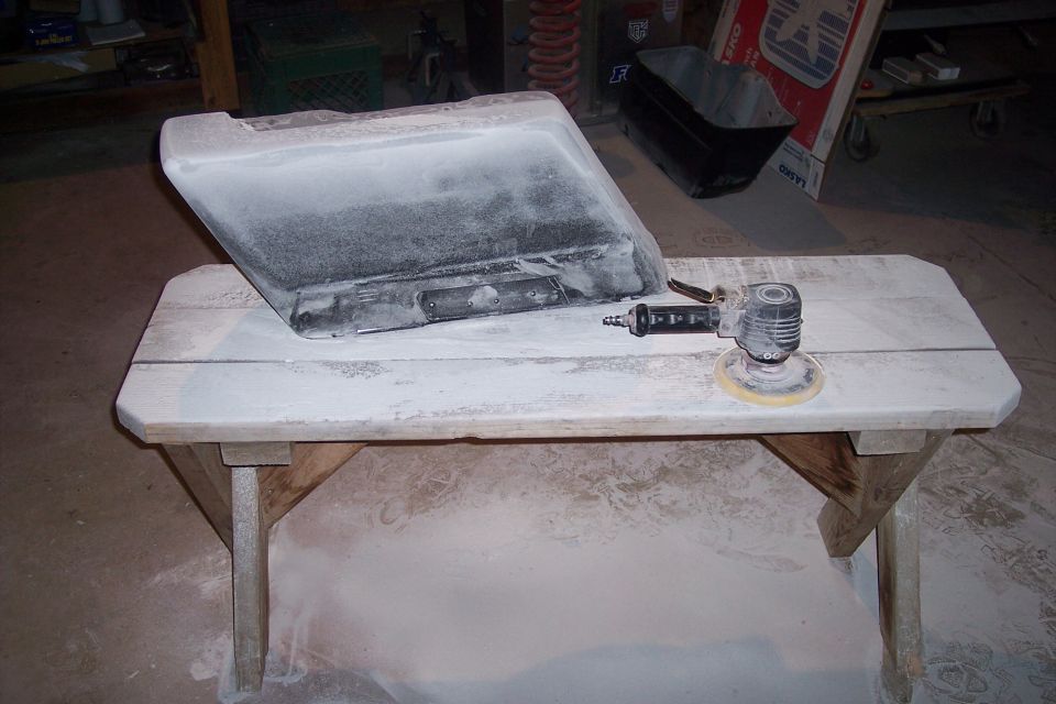 Motorcycle saddlebag covered in dust on a wooden table with a sander