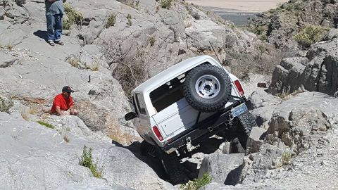 1979 Ford Bronco - A white SUV navigates a challenging rocky trail, with onlookers observing the difficult ascent.