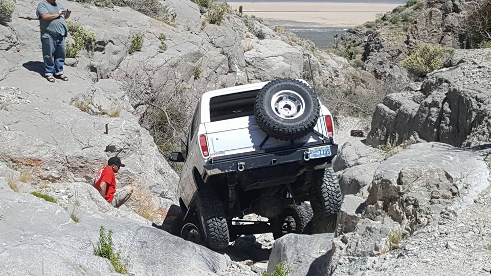 White 1979 Ford Bronco navigating a rocky trail, spare tire mounted on rear