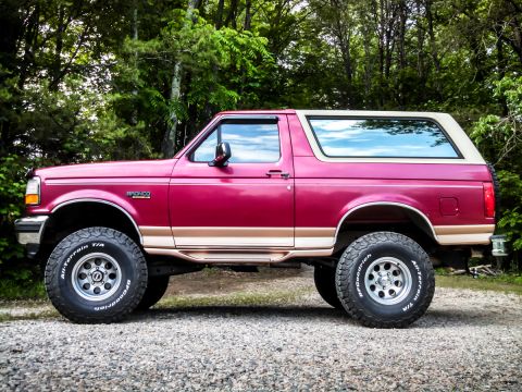 1995 Ford Bronco - This red Ford Bronco, seen from the side, is lifted and equipped with off-road tires.