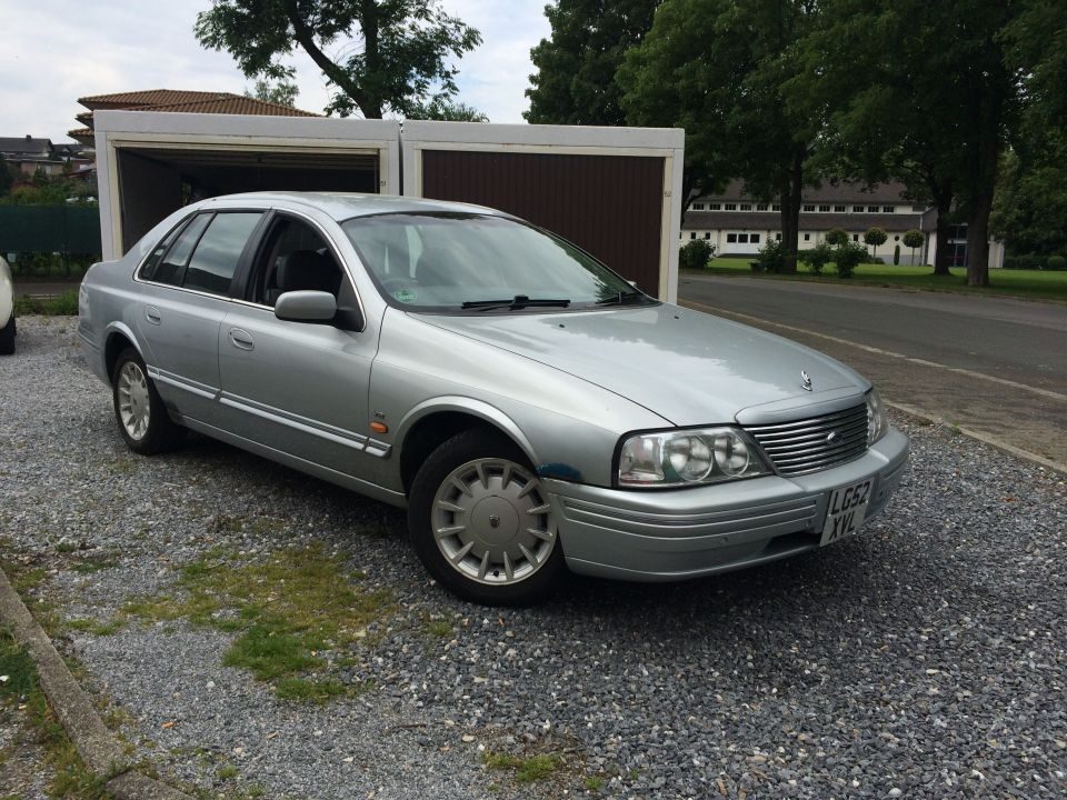Silver sedan parked on gravel lot, garage in background. License plate visible