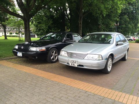 1999 Ford Fairlane - Two sedans, a silver Ford Falcon and a black Mercury Grand Marquis, are parked outdoors.