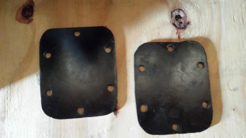 1982 Ford F-100 - Two black metal plates with bolt holes are shown on a wooden background.