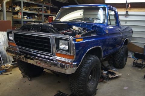 1979 Ford Bronco - This blue pickup truck is in a garage with its hood up, showing the engine bay.
