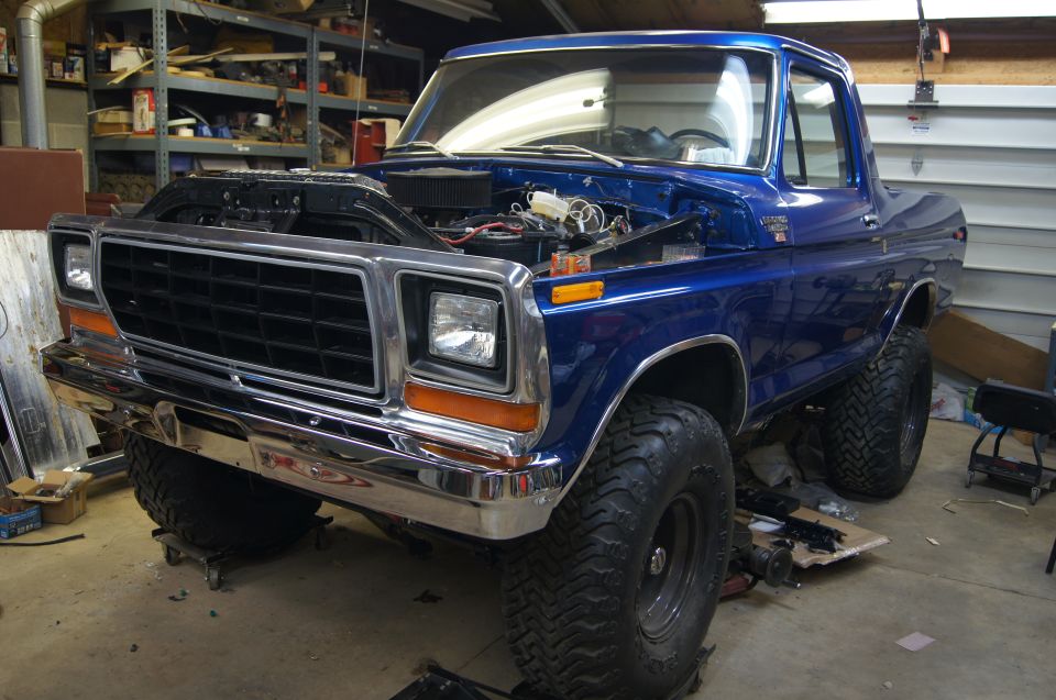 Blue pickup truck with hood open, sitting in a garage. It has large tires and chrome bumper