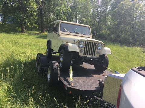 1986 Jeep Wagoneer - Tan Jeep CJ-5 loaded onto a trailer in a grassy area.