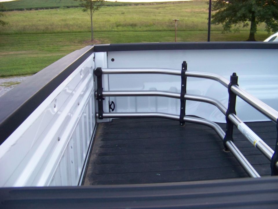 Truck bed with chrome cargo bars installed. A white truck is partially visible in the background