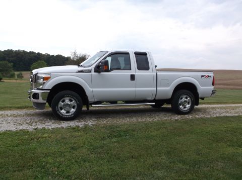 2011 Ford F-250 - This white 2011 Ford F-250 Super Duty pickup truck is shown from the side, parked on a gravel driveway.