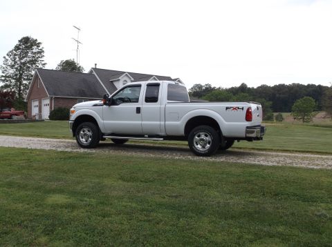 2011 Ford F-250 - A white Ford F-250 Super Duty pickup truck is parked on a gravel driveway near a house and trees.