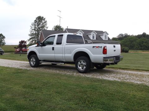 2011 Ford F-250 - A white 2011 Ford F-250 truck is parked on a gravel driveway in front of a house.