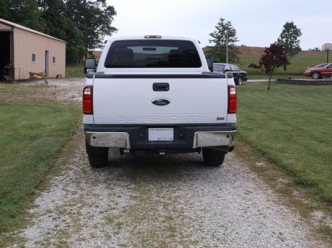 2011 Ford F-250 - White 2011 Ford F-250 Super Duty pickup truck seen from the rear on a gravel driveway.