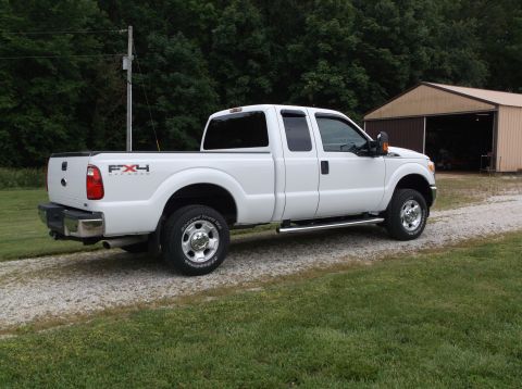 2011 Ford F-250 - A white 2011 Ford F-250 Super Duty pickup truck is parked on a gravel driveway next to a barn.