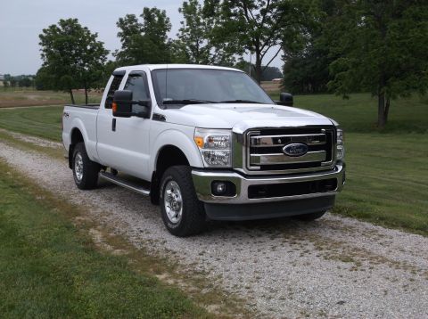 2011 Ford F-250 - A white 2011 Ford F-250 pickup truck is parked on a gravel driveway with a grassy field and trees in the background.