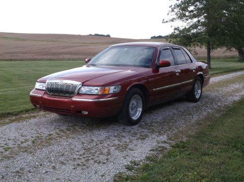 1999 Mercury Grand Marquis - A red 1999 Mercury Grand Marquis is parked on a gravel driveway with a field in the background.
