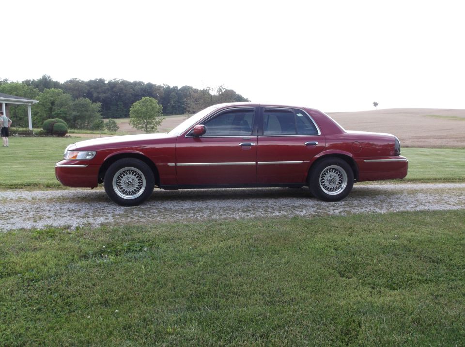 red sedan parked on gravel driveway, house and trees in background