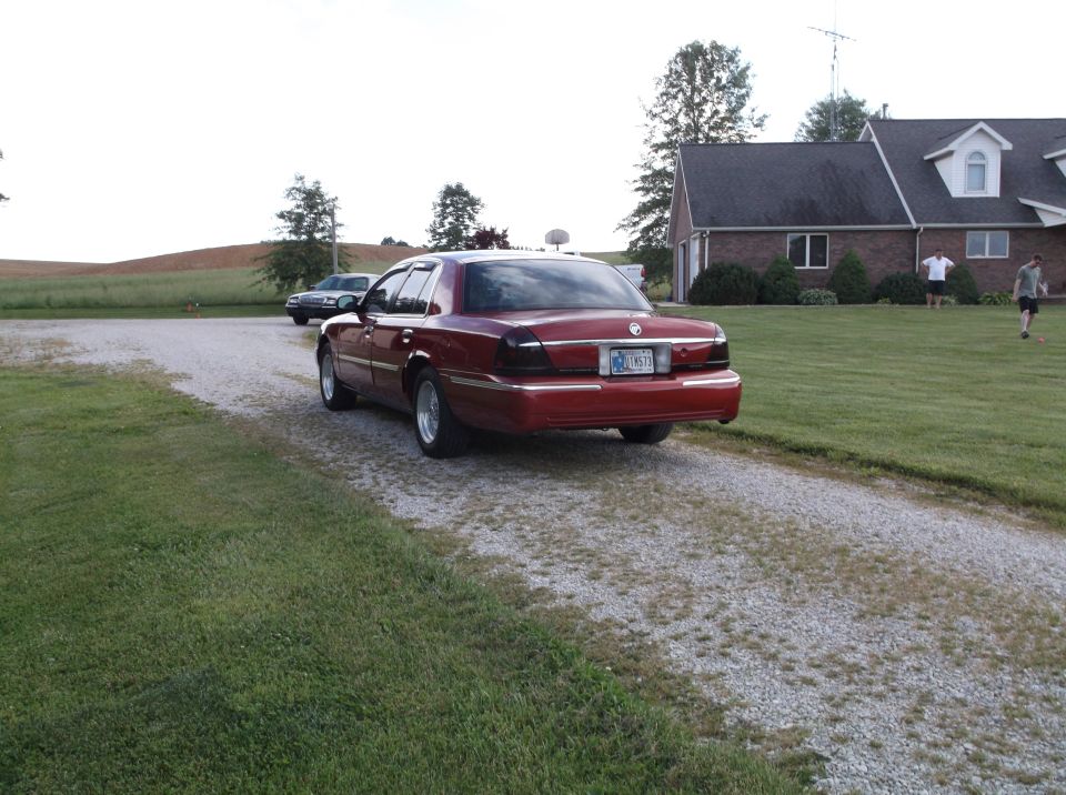 red sedan parked on gravel driveway, another car in background, house and yard to the right