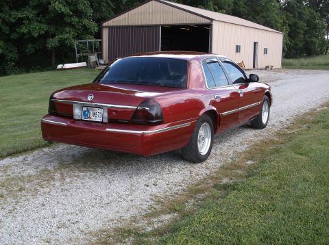 1999 Mercury Grand Marquis - This 1999 Mercury Grand Marquis features a deep red paint job and aftermarket wheels, seen from the rear.
