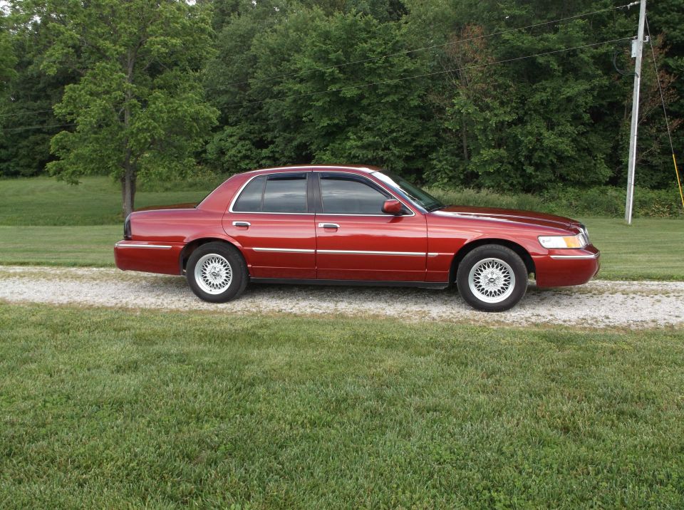 Red 1999 Mercury Grand Marquis sedan parked on a gravel driveway, side view