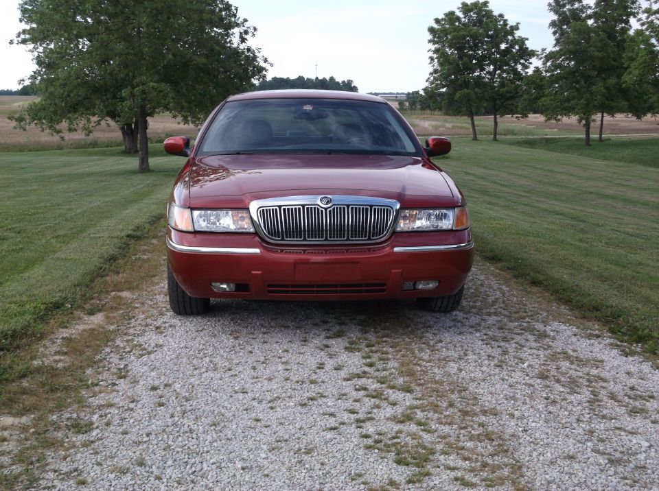 Red Mercury Grand Marquis parked on a gravel driveway, front view